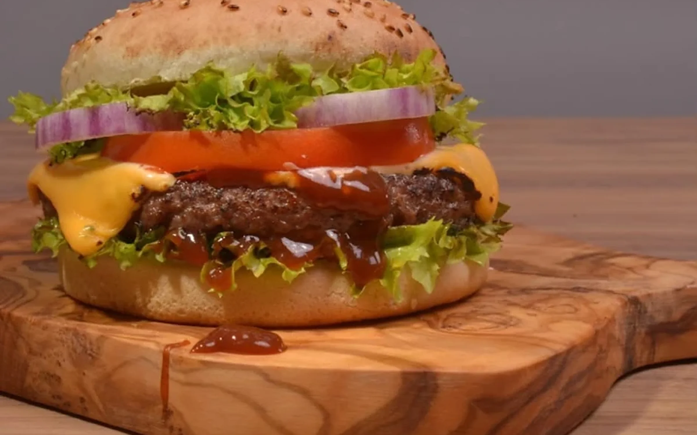 Saftiger Cheeseburger mit Salat, Tomate und Zwiebel auf einem Olivenholzbrett